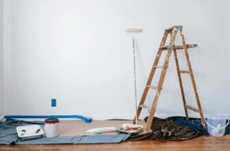 A room prepared for renovation with a ladder, paint supplies, and drop cloth.