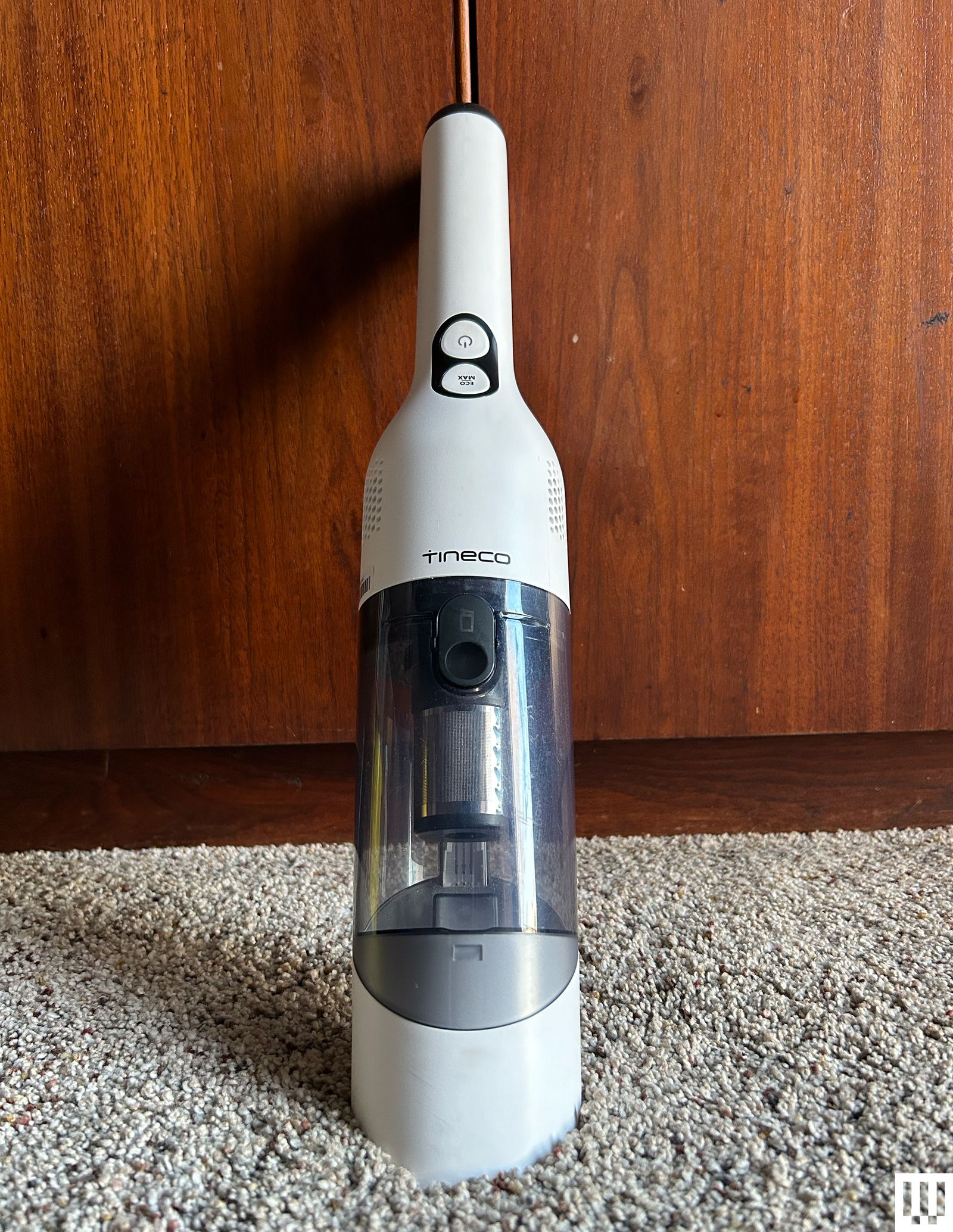 Tineco Go Mini Cordless handheld vacuum leaning against a wooden panel and carpet