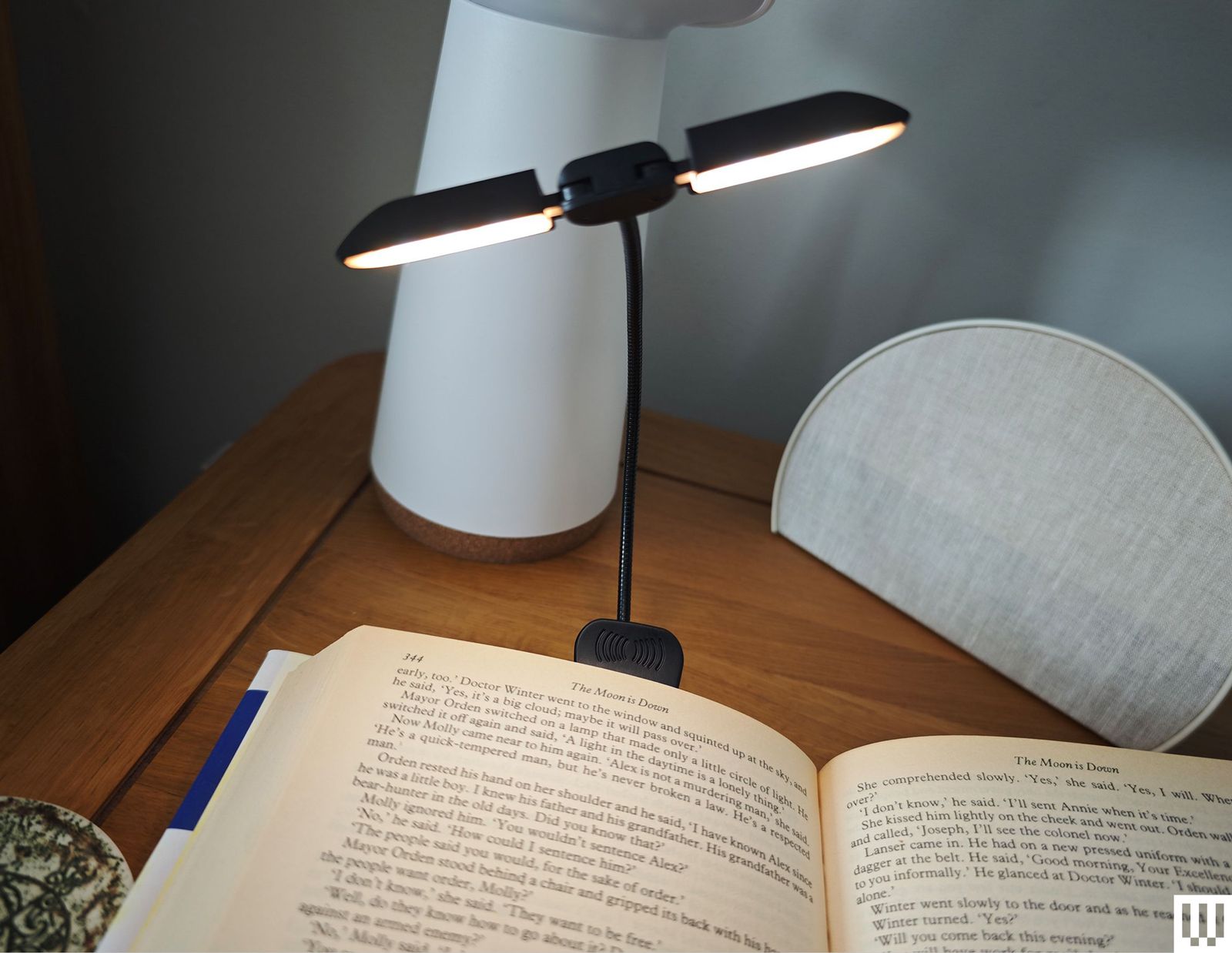 A book opened on a wooden nightstand with a thin twosided light clipped to the book
