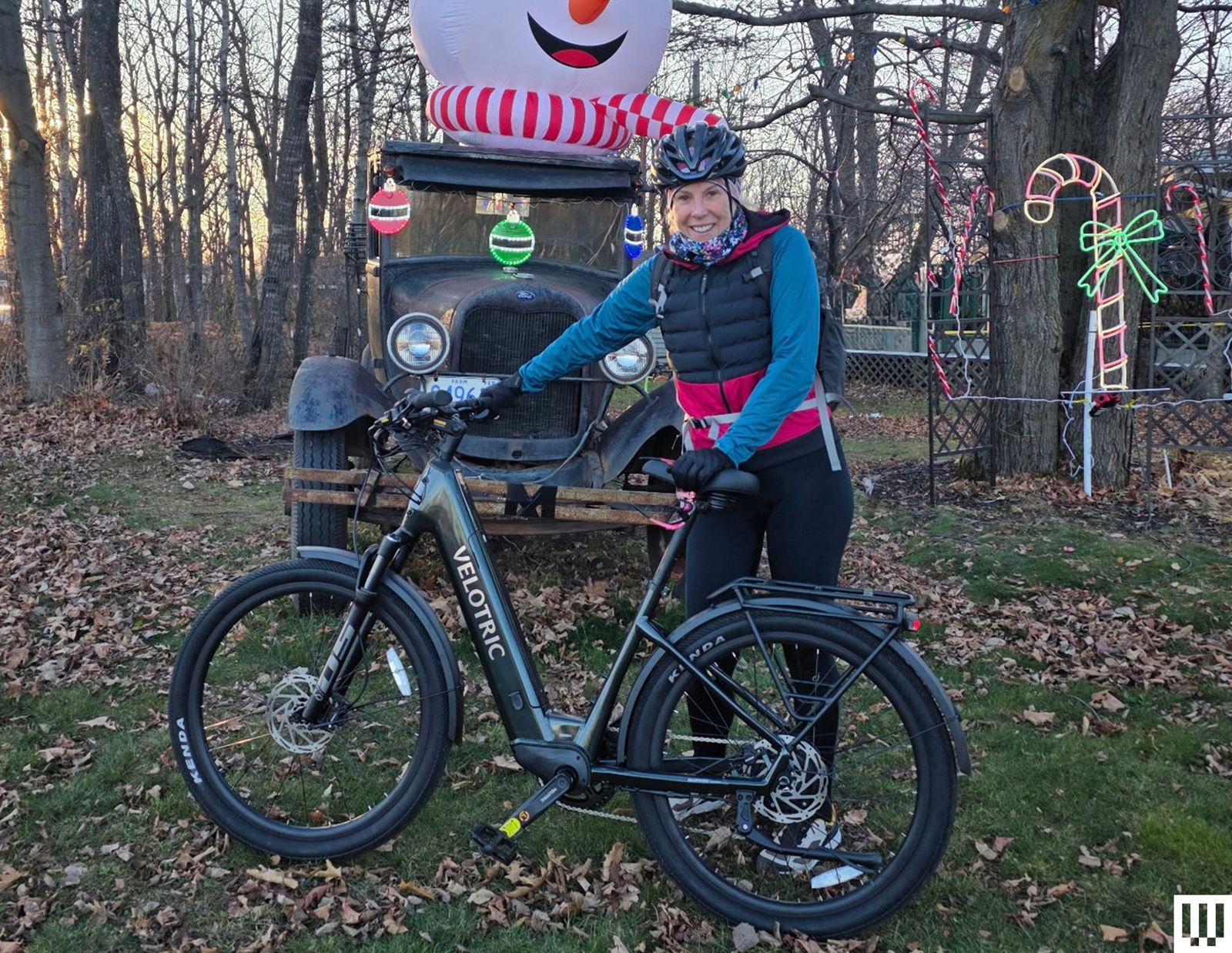 Person standing beside black Velotric Discover 2 Electric Bike with holiday decorations in the woods in the back
