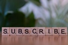 Close-up of the word 'SUBSCRIBE' spelled with wooden letter tiles on a table.