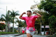 Smiling athlete in pink shirt flexing muscles while running a race outdoors.