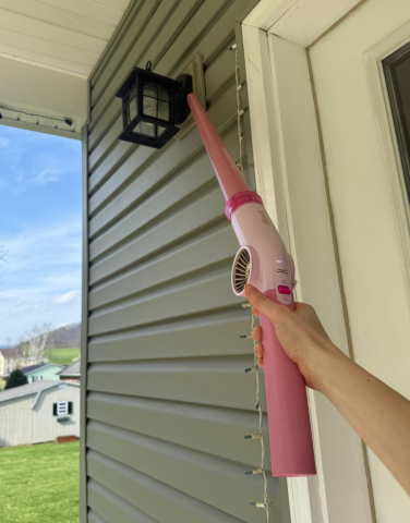 Leah using Shark BlastBoss to blow spiderwebs off of lamp on side of house