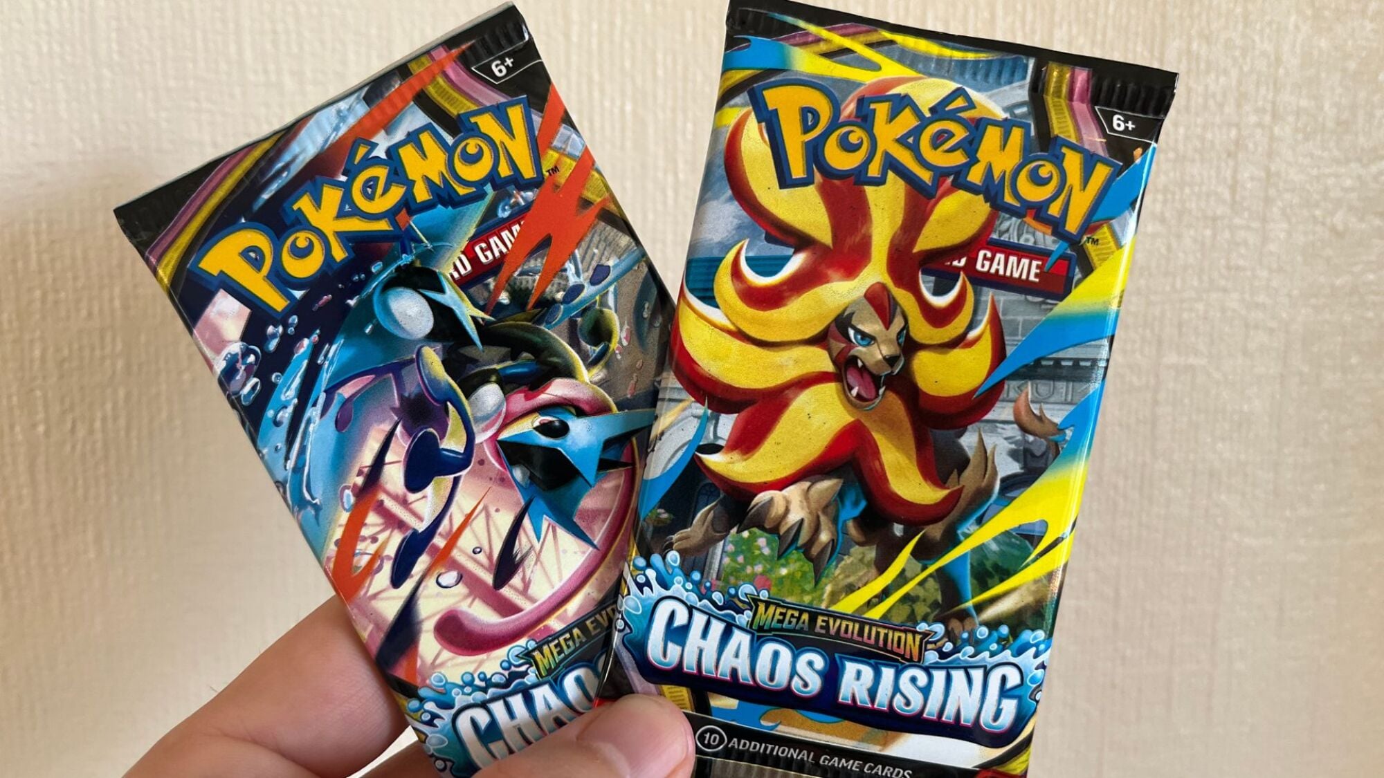 A hand holding two packs of Chaos Rising Pokemon cards.