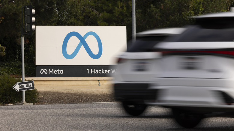 A photo showing Meta's sign at 1 Hacker way with cars driving by