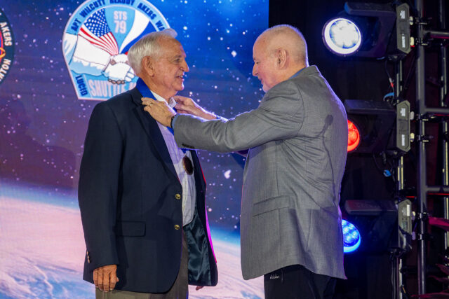 Two men in business suits are pictured as one presents a medal to the other.