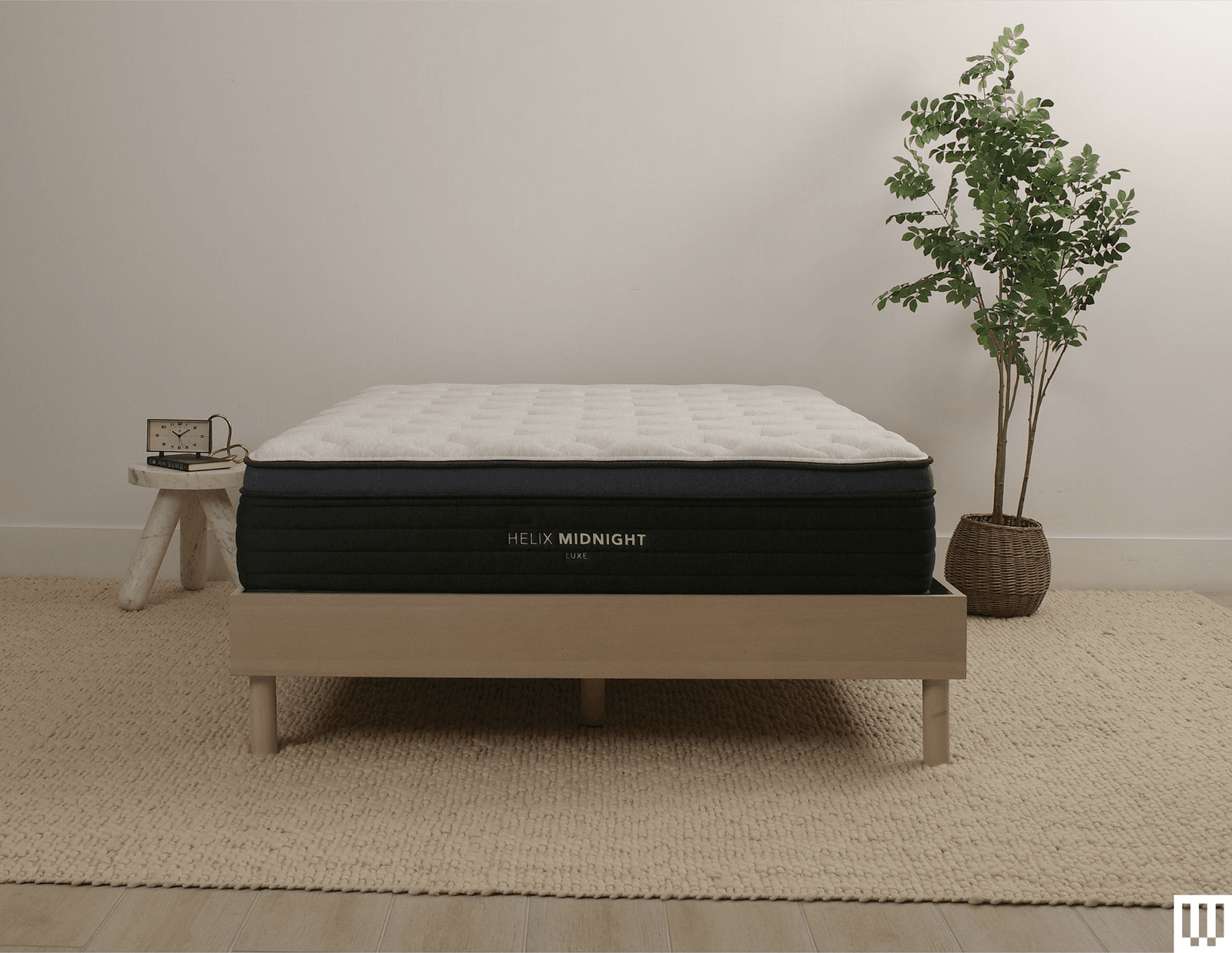 Helix Sleep Midnight Luxe a white mattress with blue trim on a minimalist wooden frame with a nightstand and potted...