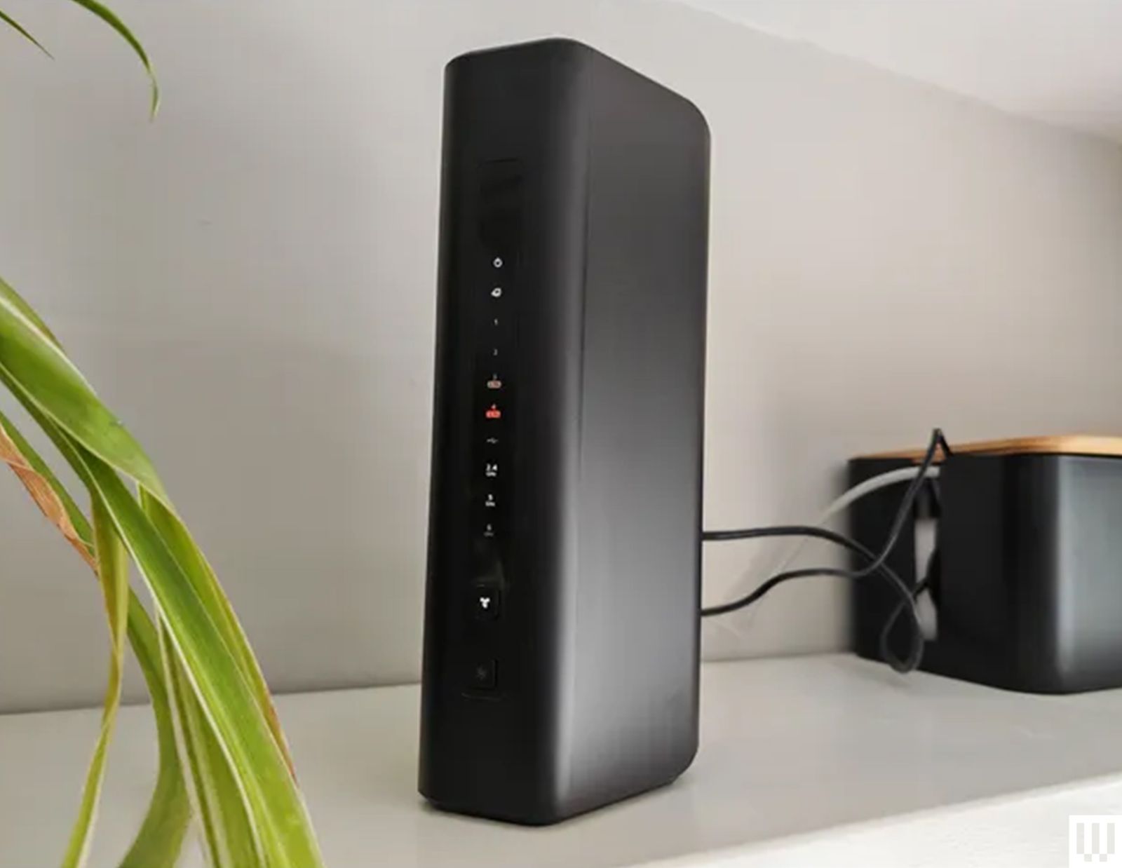 Netgear Nighthawk RS300 wifi router a black narrow device sitting on a white shelf with 2 wires coming from the back