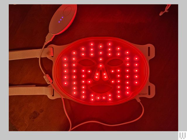 Flat facial mask with interior red lights, connected to a plug and has 2 straps