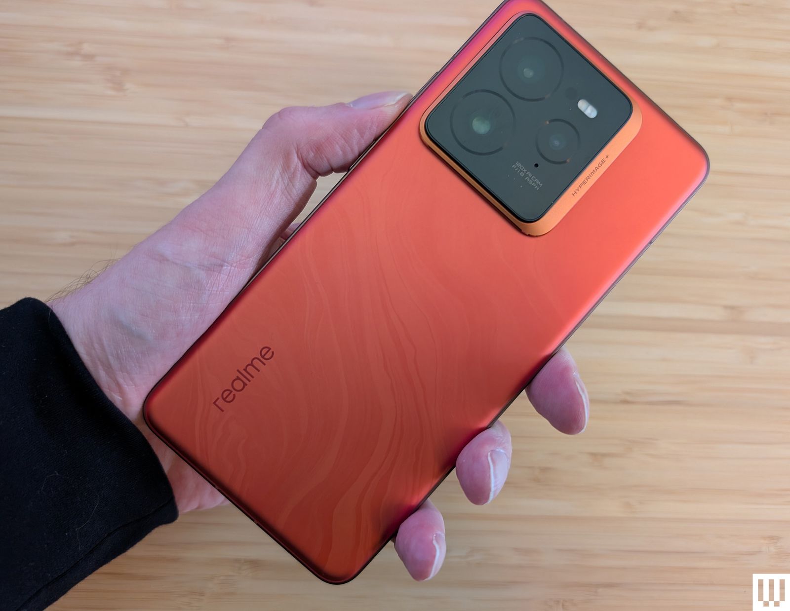 Hand holding a Realme G.T.7. Pro an orange phone with large camera lenses