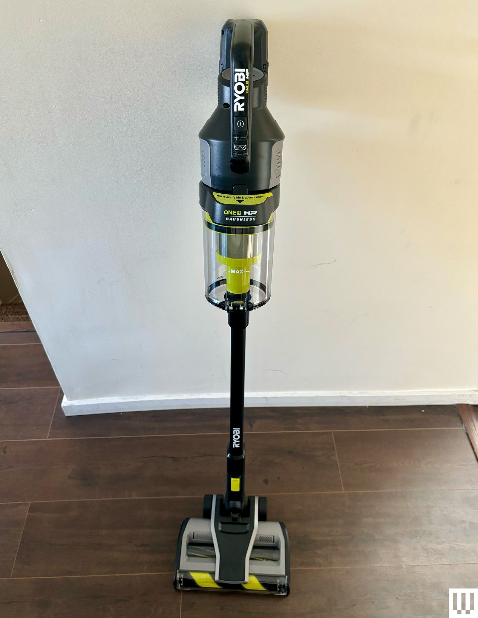 Ryobi 18V One Plus HP Stick Vacuum leaning against a white wall and dark brown floor