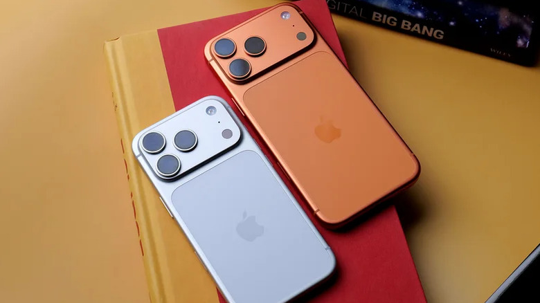 Two iPhones, on a book, on an orange table, on a floor, on a building, on the ground.