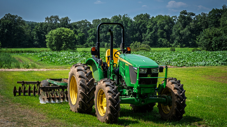 Photo of a John Deere tractor stopped on a grass lawn, with a garden plot in the midground and trees in the background.