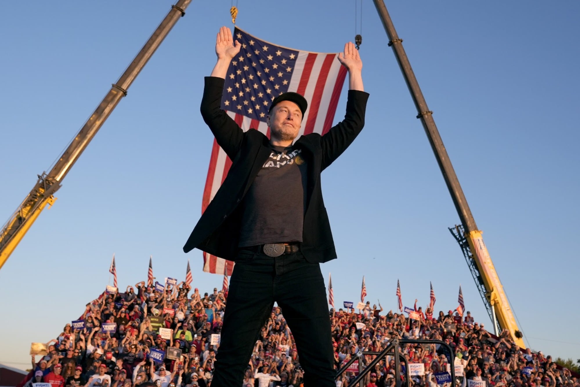 Elon Musk stands before an American flag.