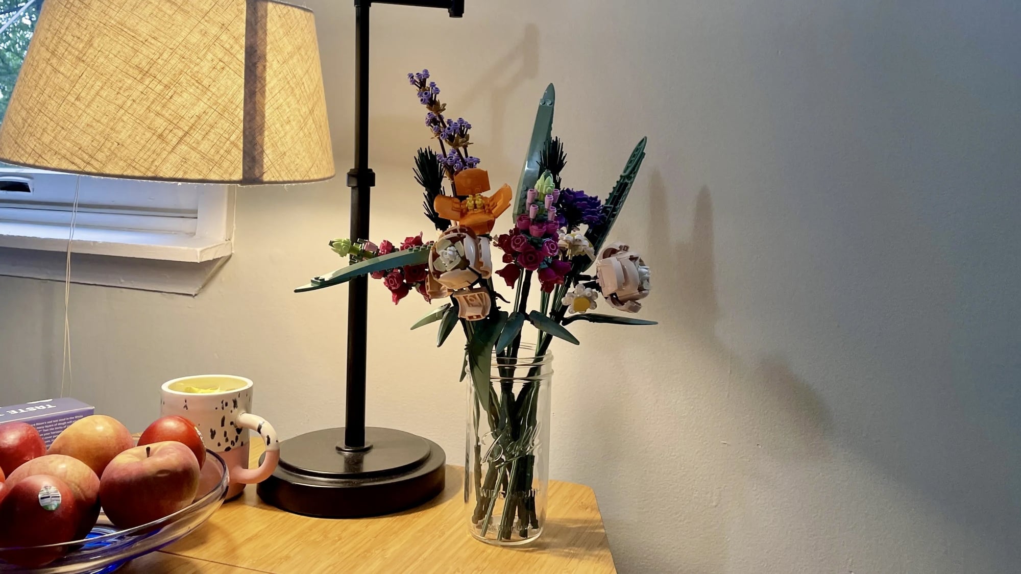 lego botanicals flower bouquet on side table next to lamp and bowl of fruit