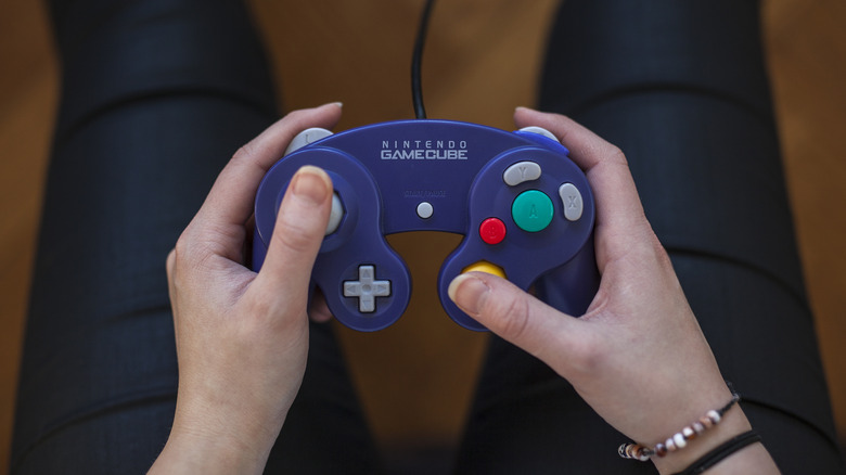 A person holding an indigo GameCube controller above their legs