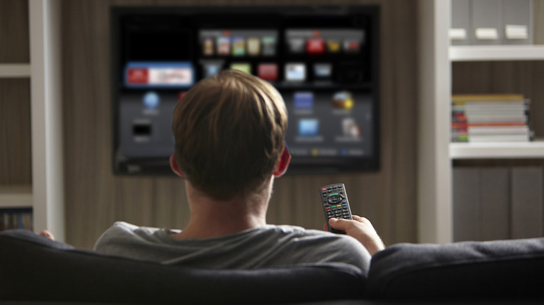 Man holding a remote and watching TV from a couch.
