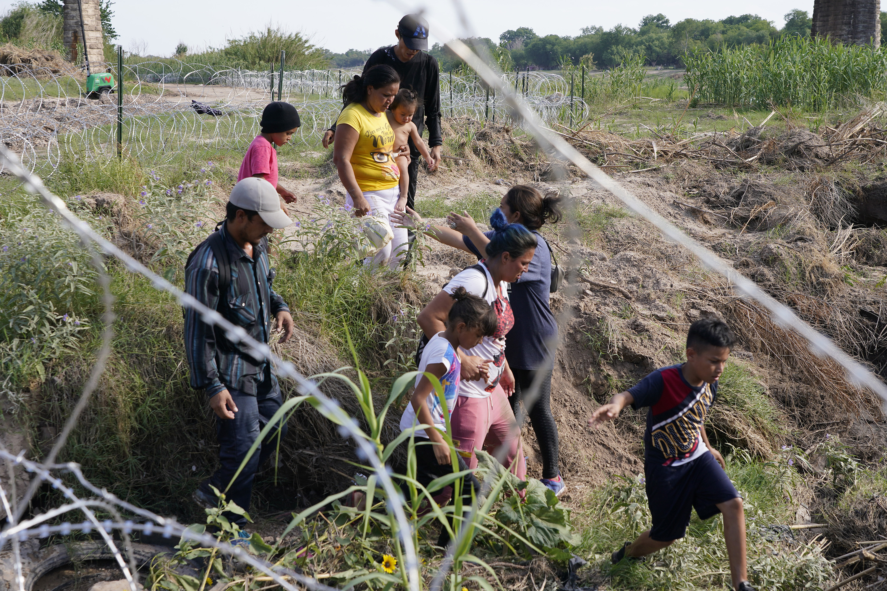 Migrants, most with children, follow a path along the concertina wire where ultimately they will placed under guard by Border Patrol after having crossed the Rio Grande on May 27, 2022 in Eagle Pass, Texas.